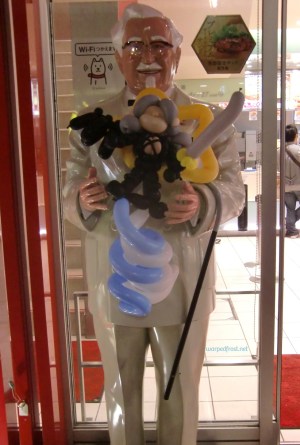 Balloon Seph in the arms of a statue of Colonel Sanders outside of a KFC