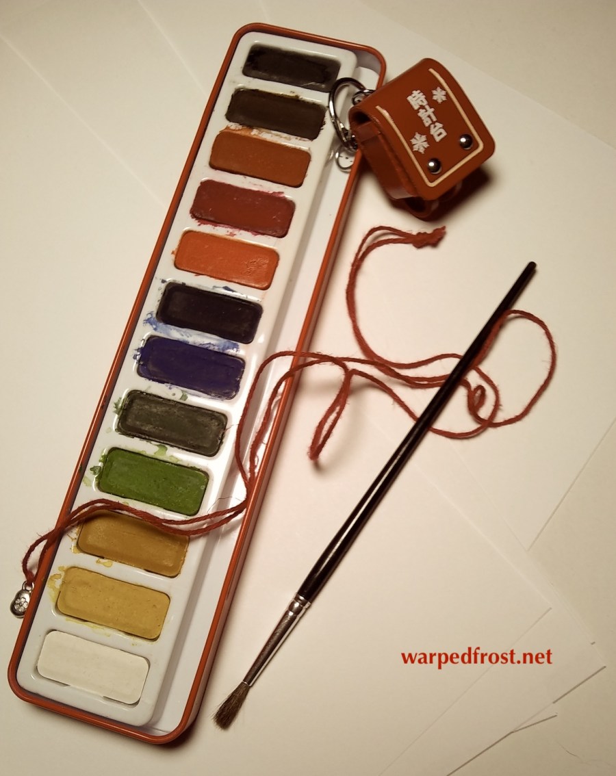 Photo of a tray of watercolor paint, brush, miniature 'randoseru' (a leather backpack Japanese elementary students have), sheets of paper, and a red string.